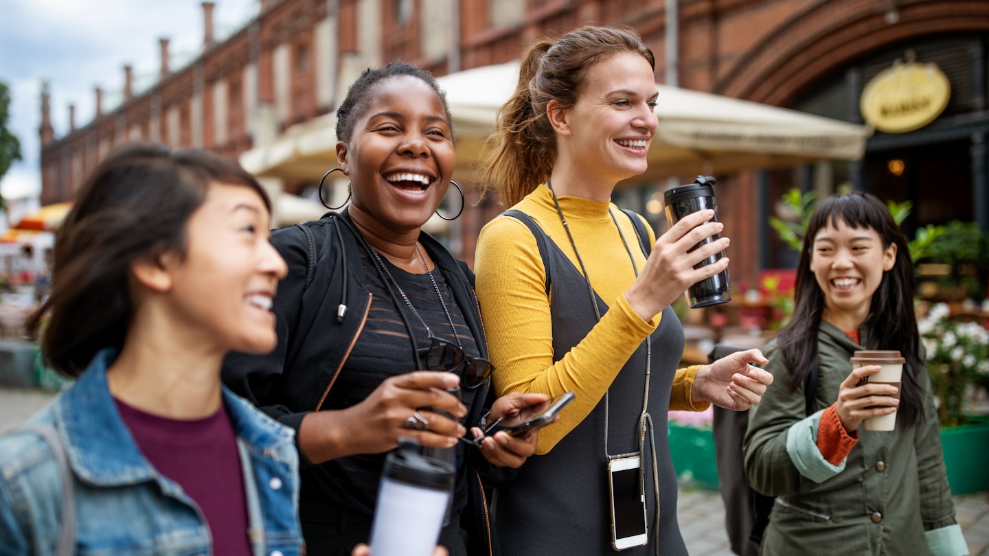 A group of friends walk through a city street holding coffee cups.